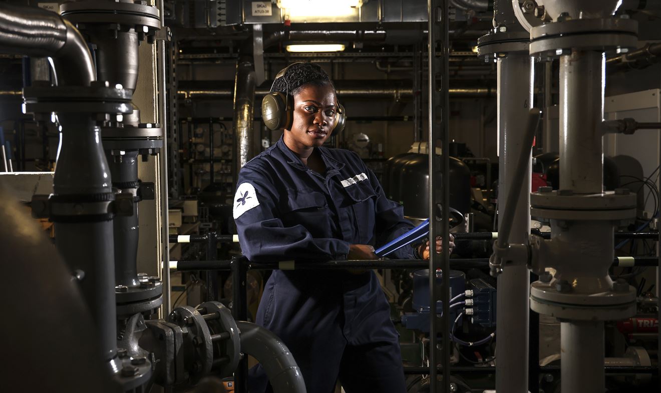 uniformed Royal Navy Mechanical Engineer checking key equipment on board aircraft carrier HMS Prince of Wales