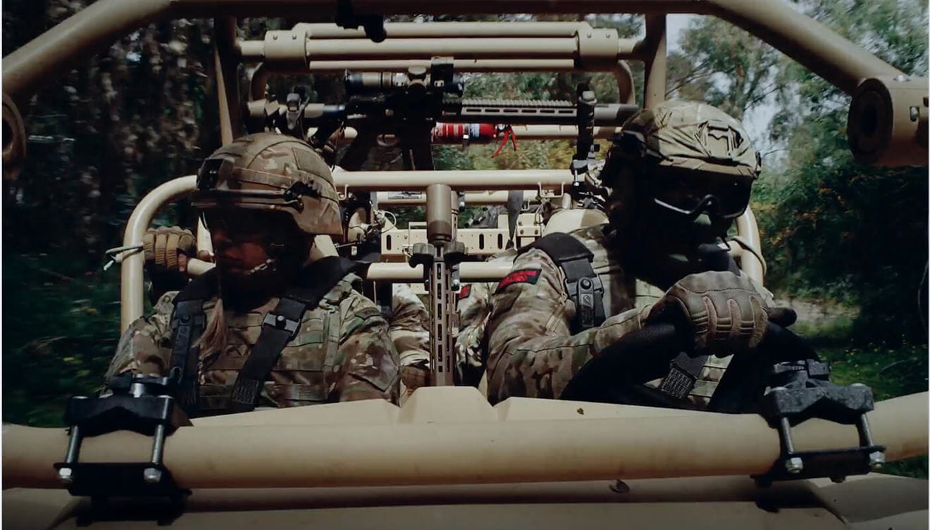 Two Royal Marines in camouflage with one of them driving a military vehicle.