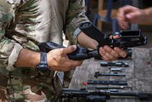 An image of some hands assembling a gun with other gun parts on a table.