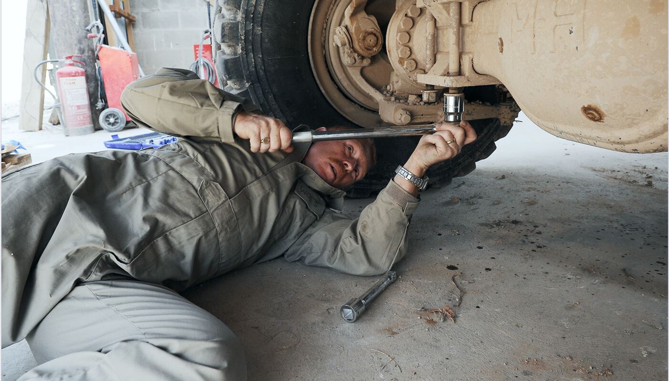 A Royal Marine mechanic laying on the floor with a tool and fixing the underside of a vehicle.