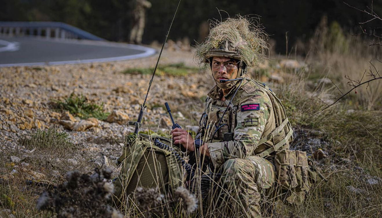 Marine commando camouflaged amongst his environment, crouching to the ground
