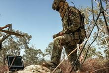 A marine commando stood over his computer tech device, in a humid environment