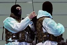 Two Royal Marines standing next to each other wearing white overalls, camouflaged vest tops and balaclavas.