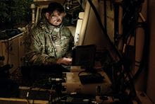 A Royal Marine sitting in the dark with the glare at a computer screen.