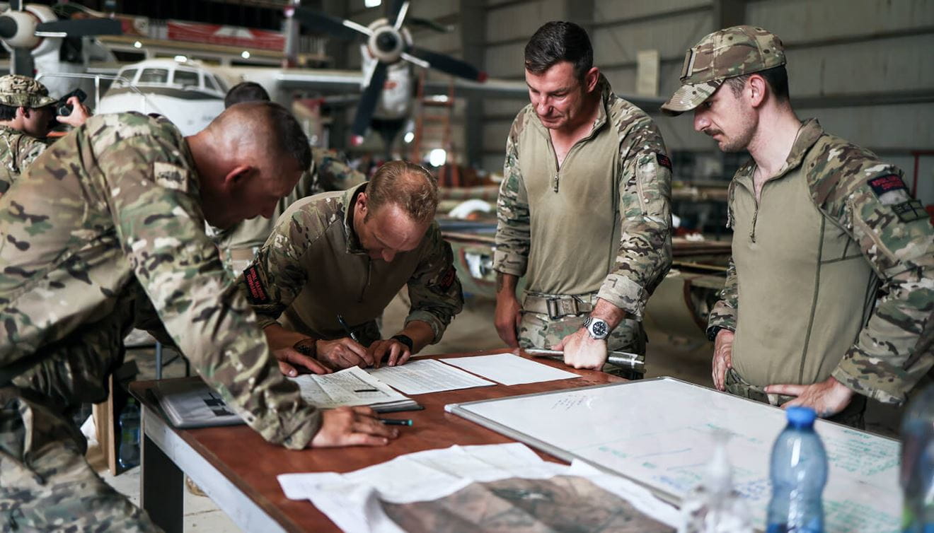 Four Royal Marines in uniform, standing around a table looking at some paperwork.