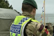 Royal marines police looking towards the sea, wearing his police high-vis vest.