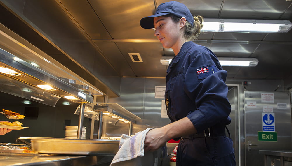 Steward carrying out their duties in the dinning hall of RFA Argus. RFA Argus personnel at work.