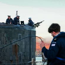 Four submariners in the background and one in the foreground holding some equipment all in uniform