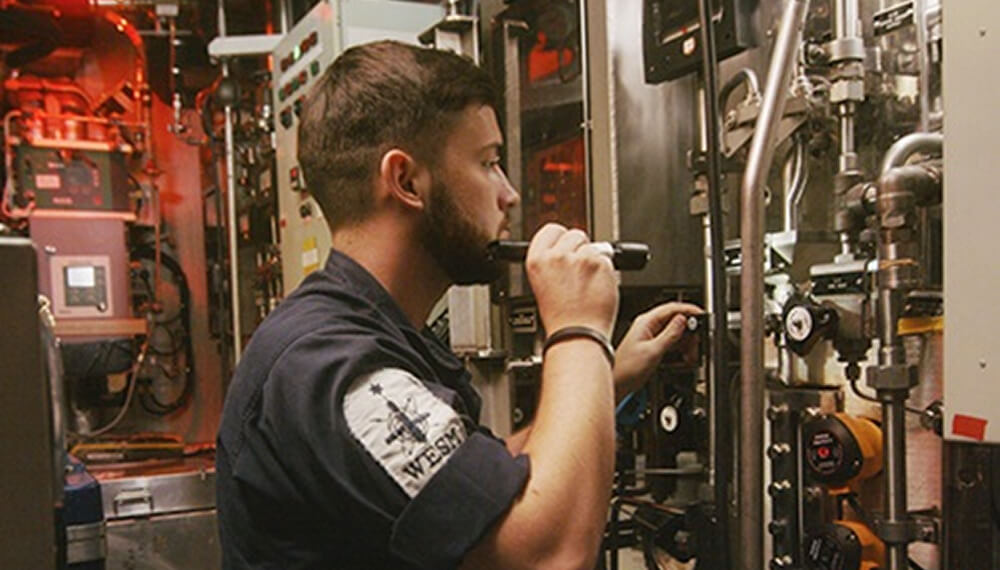 Submariner working in tight mechanical space surrounded by wires and pipes