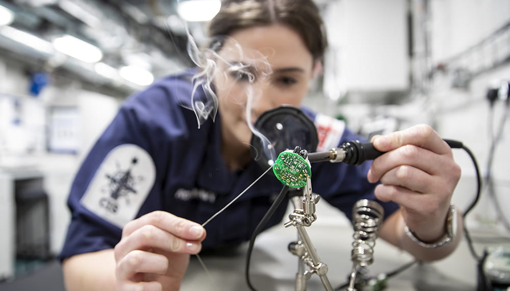 brown haired and uniformed Communication Information Systems weapons engineer soldering telephone handset on board HMS Queen Elizabeth aircraft carrier
