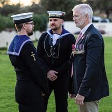 Two Navy sailors in uniform with one man wearing a suit with medals.