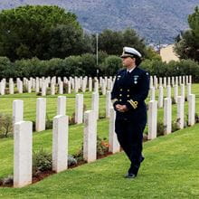 A female Navy member wearing a uniform walking among some gravestones.