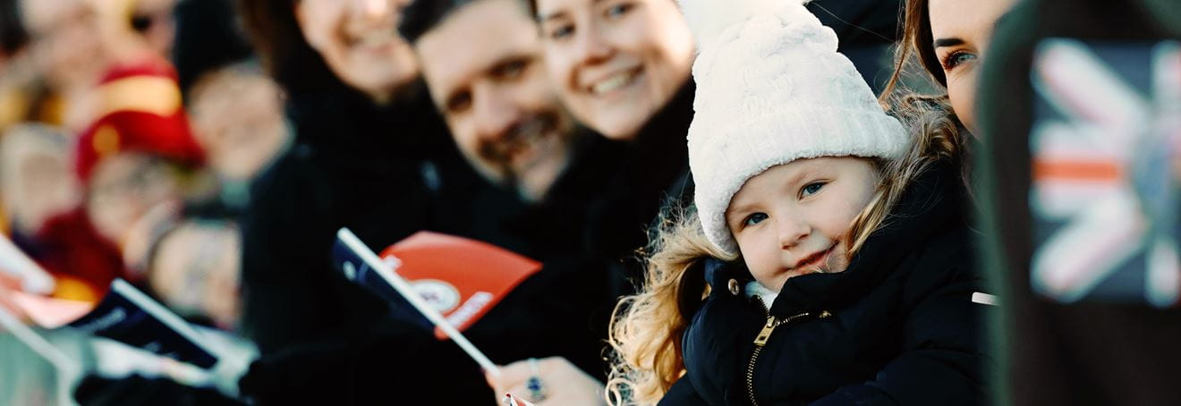 A young girl in the crowd smiles at the camera and waves a homecoming flag
