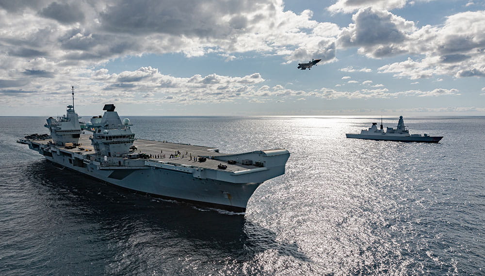 Royal-Navy-Global-Operations-03-North-Atlantic Fighter Jet coming in to land on HMS Queen Elizabeth Aircraft Carrier with Type 45 frigate in background