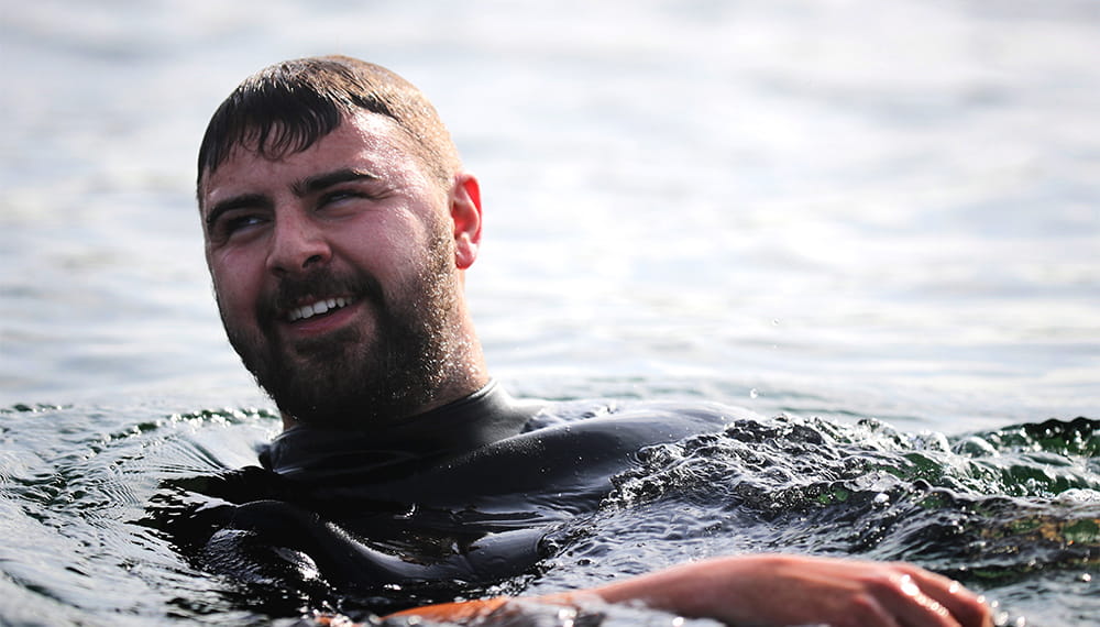Male swimmer in a wetsuit smiling as he floats on his back in the sea