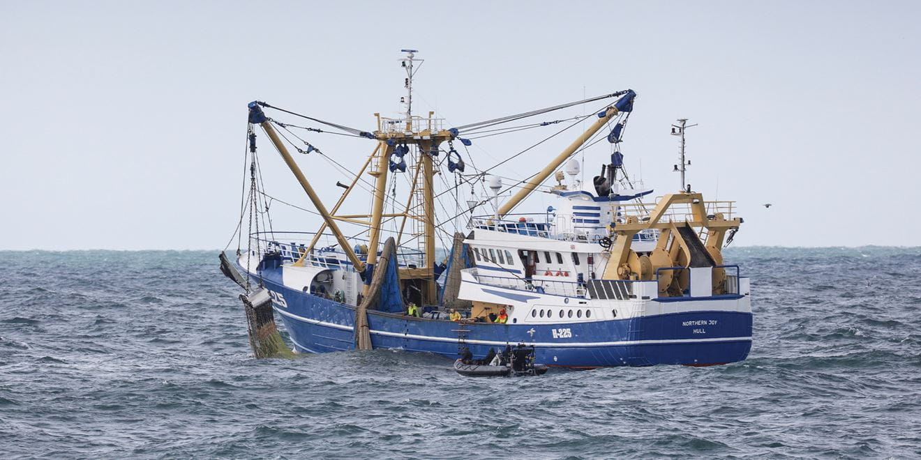 A black rib boat approaches a white and blue fishing vessel on its port side