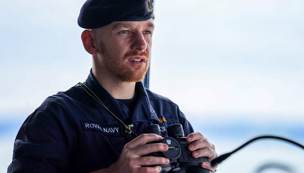Royal Navy Sailor with binoculars in his hands stares past the camera