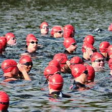 A large group of swimmers in red swim caps and goggles tred water 