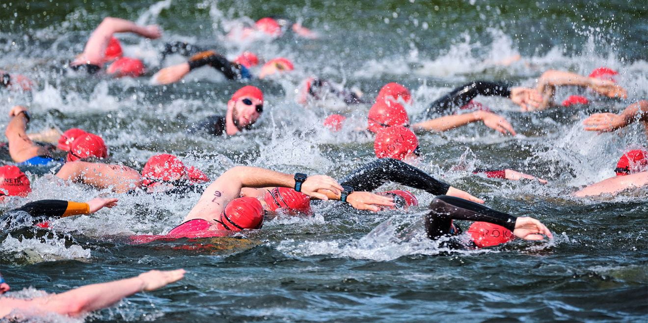 Lots of people, wearing red swim caps, participate in a swim race in the sea