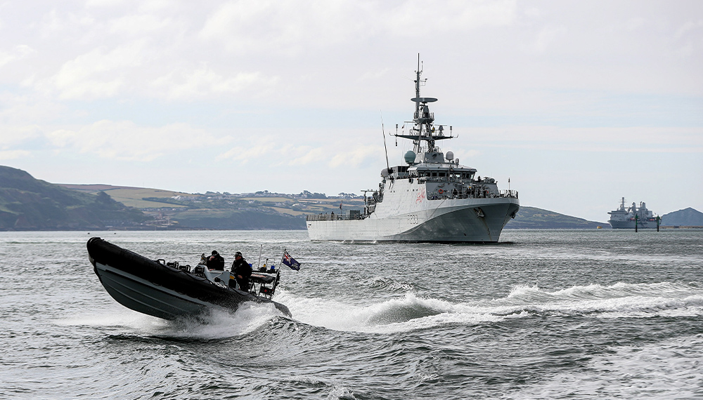 A black rib boats passes at speed in front of HMS Tamar, a River class ship