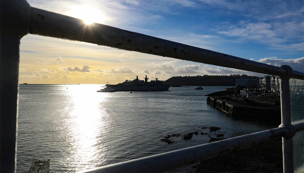 a Navy ship can be seen in the distance as the sun shines on the sea