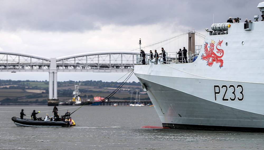 A small black rib boat giving personnel aboard the HMS Tamar rope to connect the two boats
