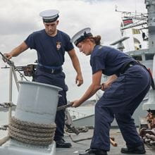 2 navy sailors fasten a rope on a Navy ship