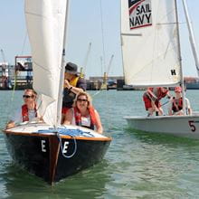 2 small sailing boats with individuals wearing life jackets sailing in port