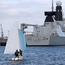 A small boat sails away from the camera toward a Daring class destroyer