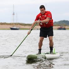 Man in red thermal and life vest paddle boarding in the sea