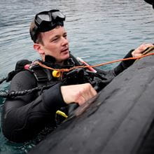 Man in black diving gear hanging onto rib boat
