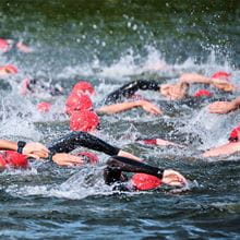 Lots of people participating in a swim race in the sea with red swim caps on