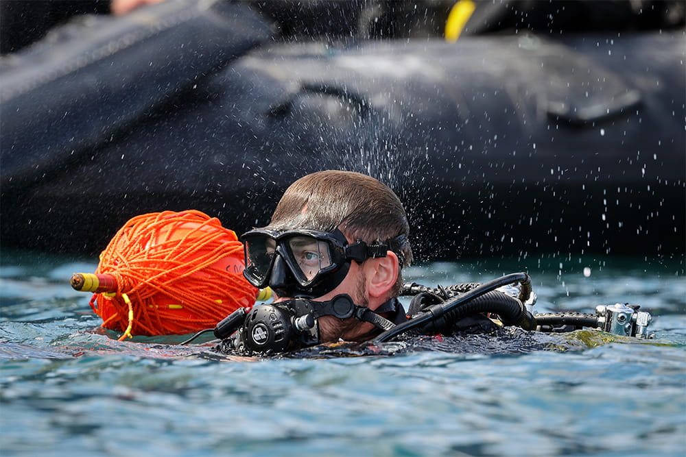 Diver with sea mask above water with an orange surface marker buoy next to him