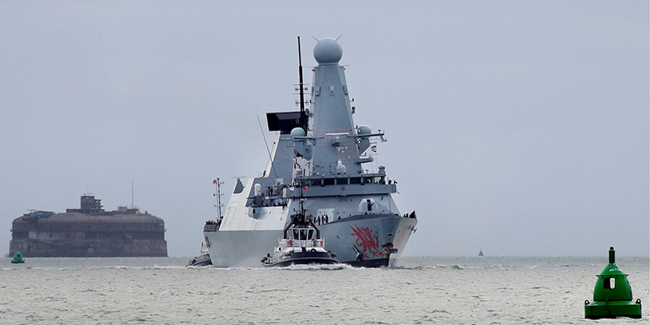 HMS Dragon sailing towards the camera with a smaller patrol boat alongside it