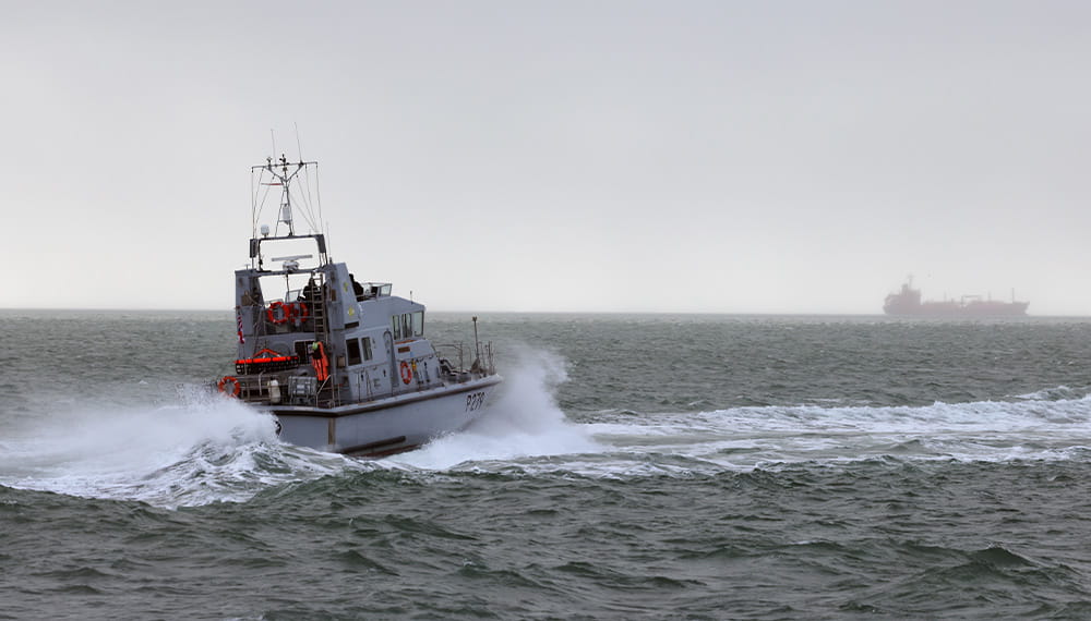 An archer class boat sails away from the camera towards a boat in the distance