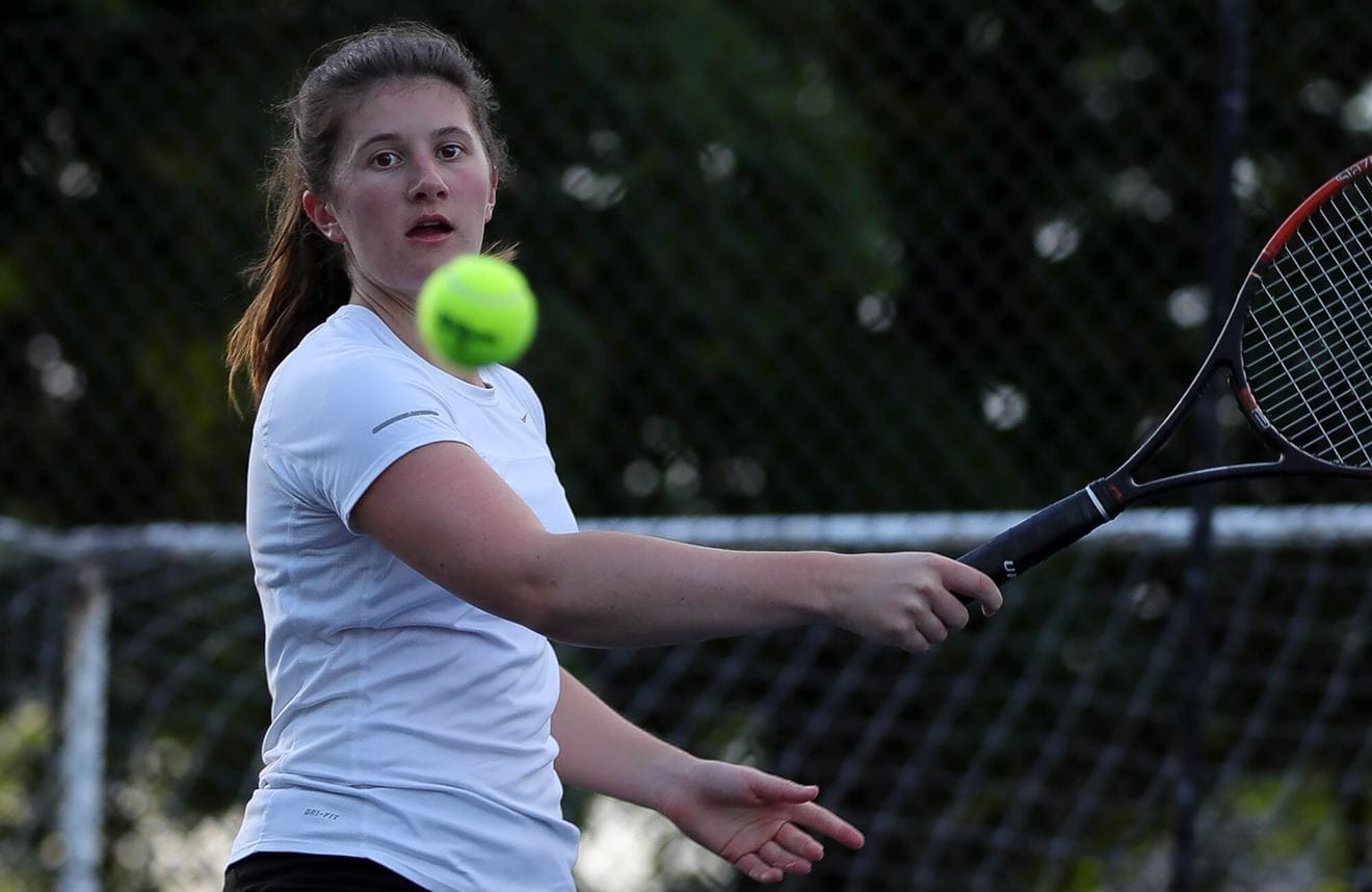 A colour photo shows a Royal Navy tennis player swinging a racket towards an incoming ball. The ball zooms into the centre of the image from the left of the frame.