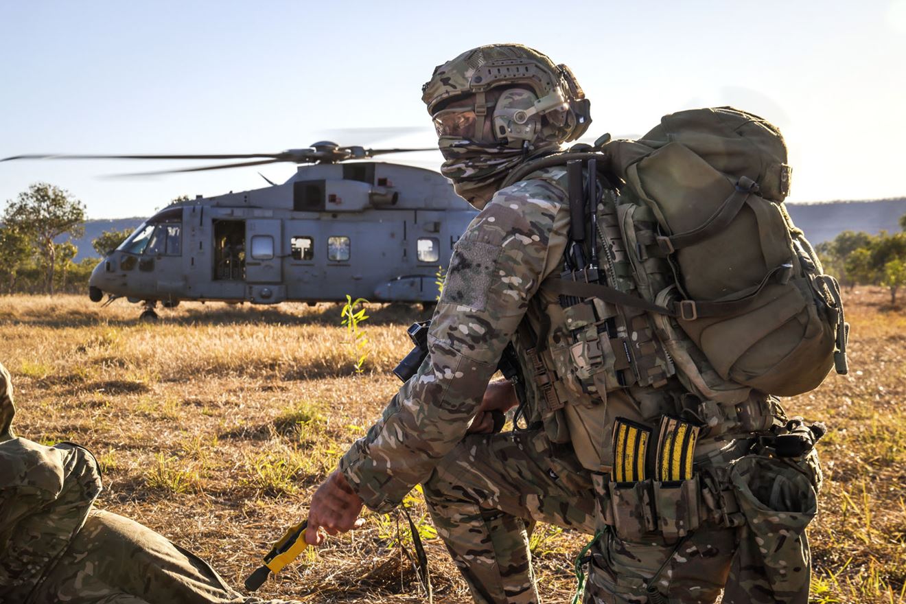 A stick of Royal Marines wait to join a Merlin in the field