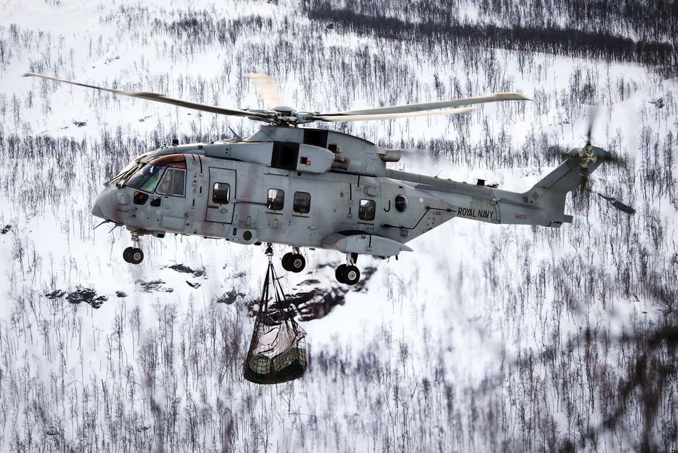 A Merlin Mk4 carries the load of logs over the snow-covered landscape