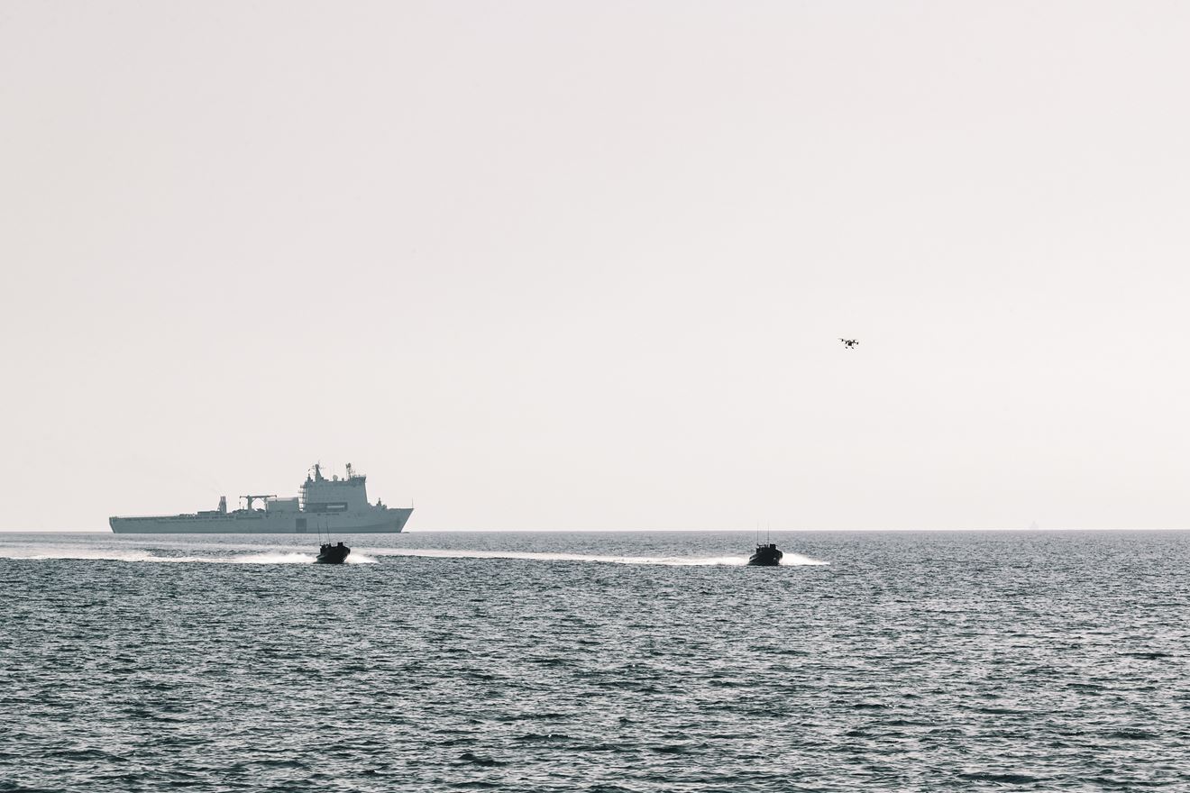 A quadcopter drone passes over RIBs carrying 42 Commando ashore from RFA Lyme Bay in the background