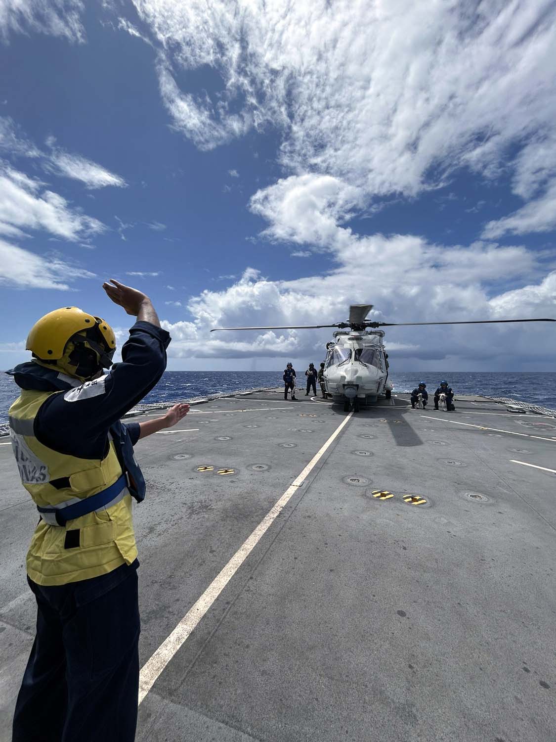 HMS Medway's flight deck officer signals to shipmates strapping a Dutch NH90 to the flight deck