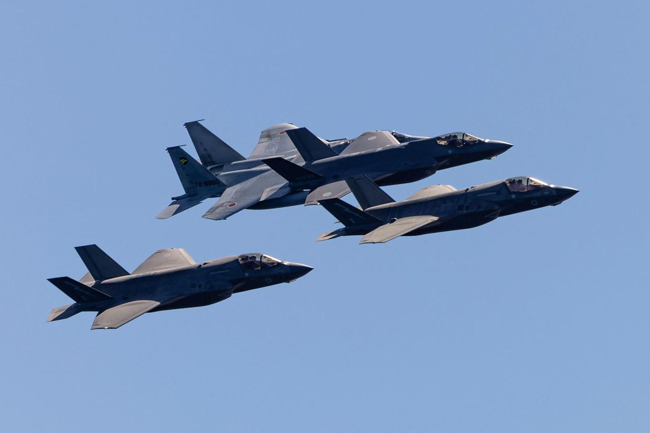 Two UK F-35Bs with a Japanaese F-15 (top left) and F-35A (top right) pass HMS Prince of Wales