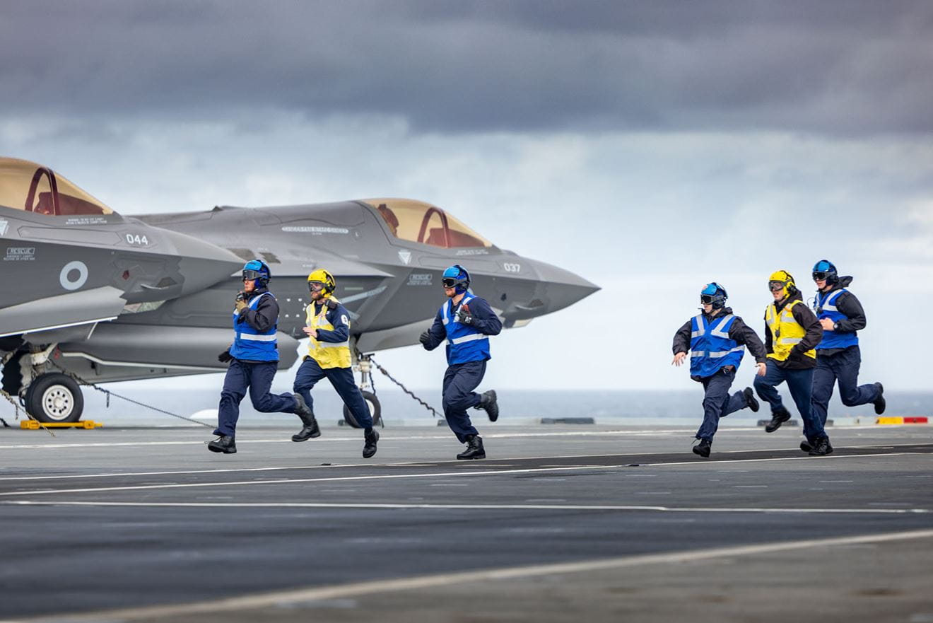 Handlers dashacross the flight deck with Lightnings lashed down