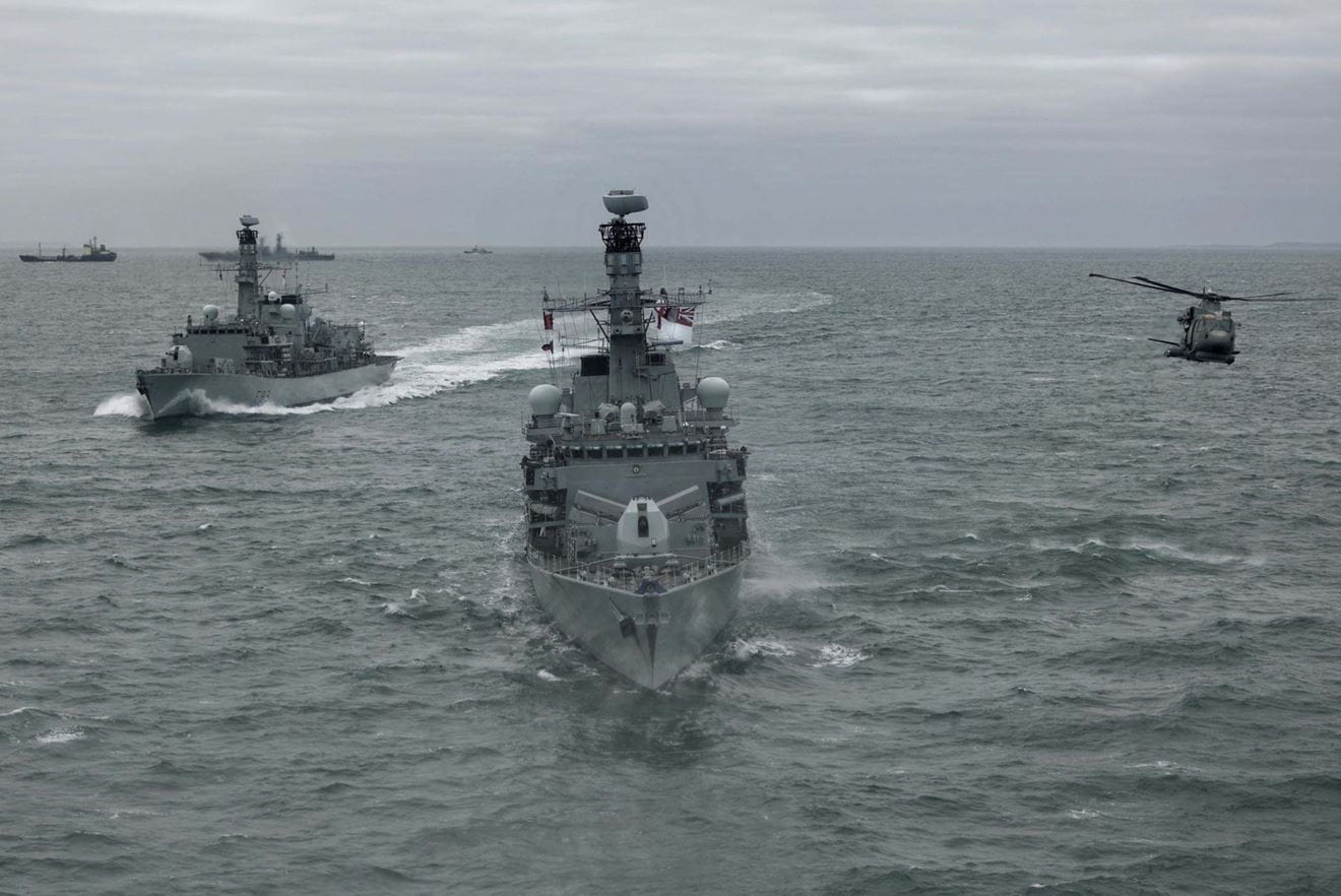 A Merlin helicopter flies alongside HMS Somerset centre as she takes over from HMS St Alba