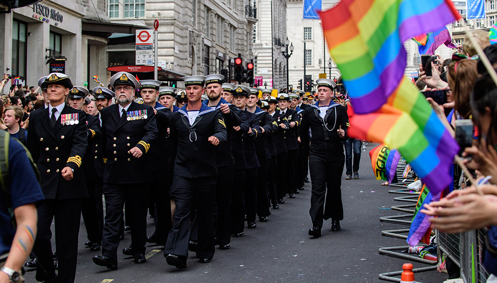 Royal-Navy-Our-People-Ops-for-all-04-lgbtq.jpg Royal Navy sailors march in front of crowd waving Rainbow flags