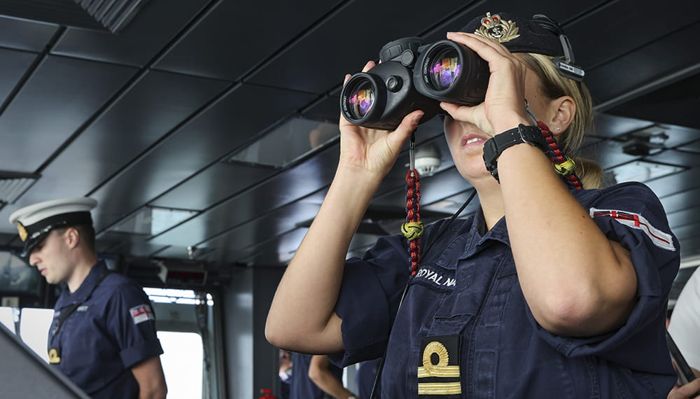 Royal-Navy-What-we-do-prevent-02-keeping-448.jpg Royal Navy officer looks through binoculars from the bridge of a ship