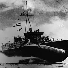 A black-and-white photo shows a torpedo firing from a British motor torpedo boat, while moving at speed.