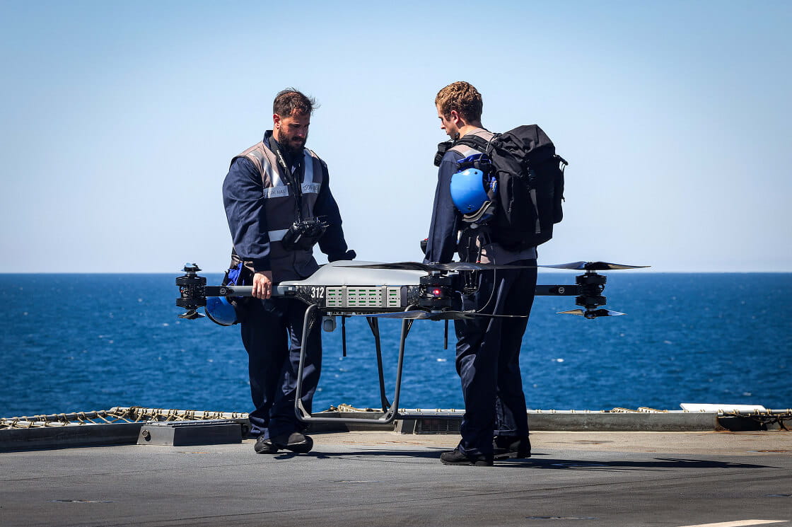 Royal Navy personnel onboard an aircraft carrier with a drone