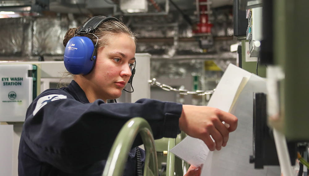 royal-navy-careers-joining-options-04 uniformed royal navy engineer wearing blue ear protectors looking at notes in engine room