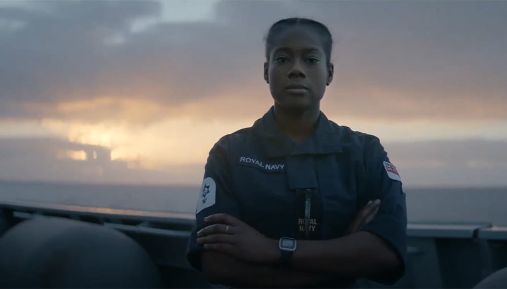 tammi on board and in blue uniform with arms crossed looking into camera with dramatic sun setting sky behind