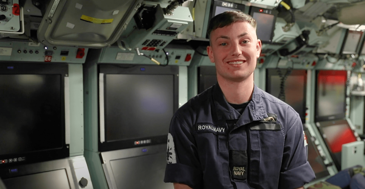 An image of a warfare sepcialist submariner in uniform in a submarine talking to a camera
